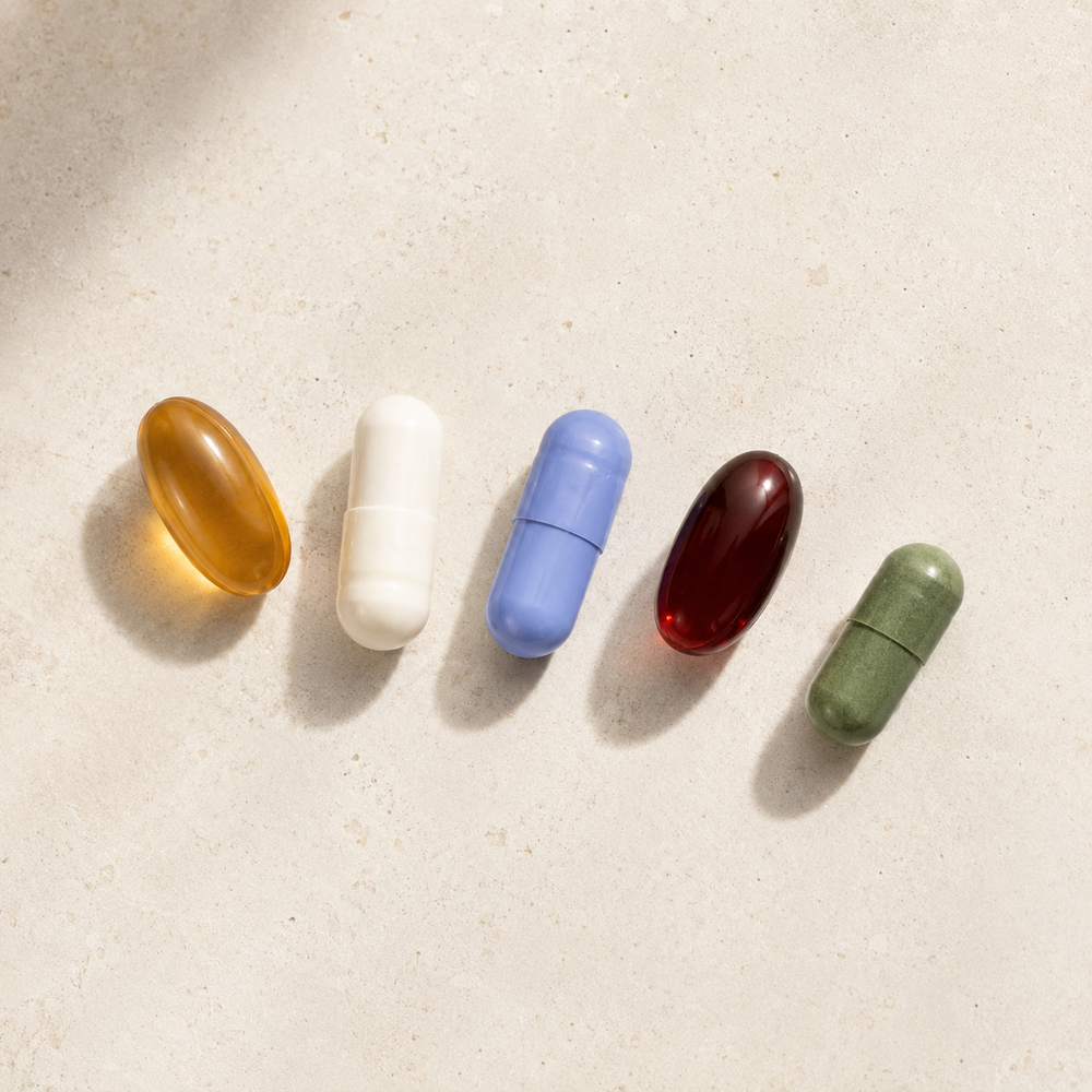 Five supplement capsules laid out on a cream surface.
